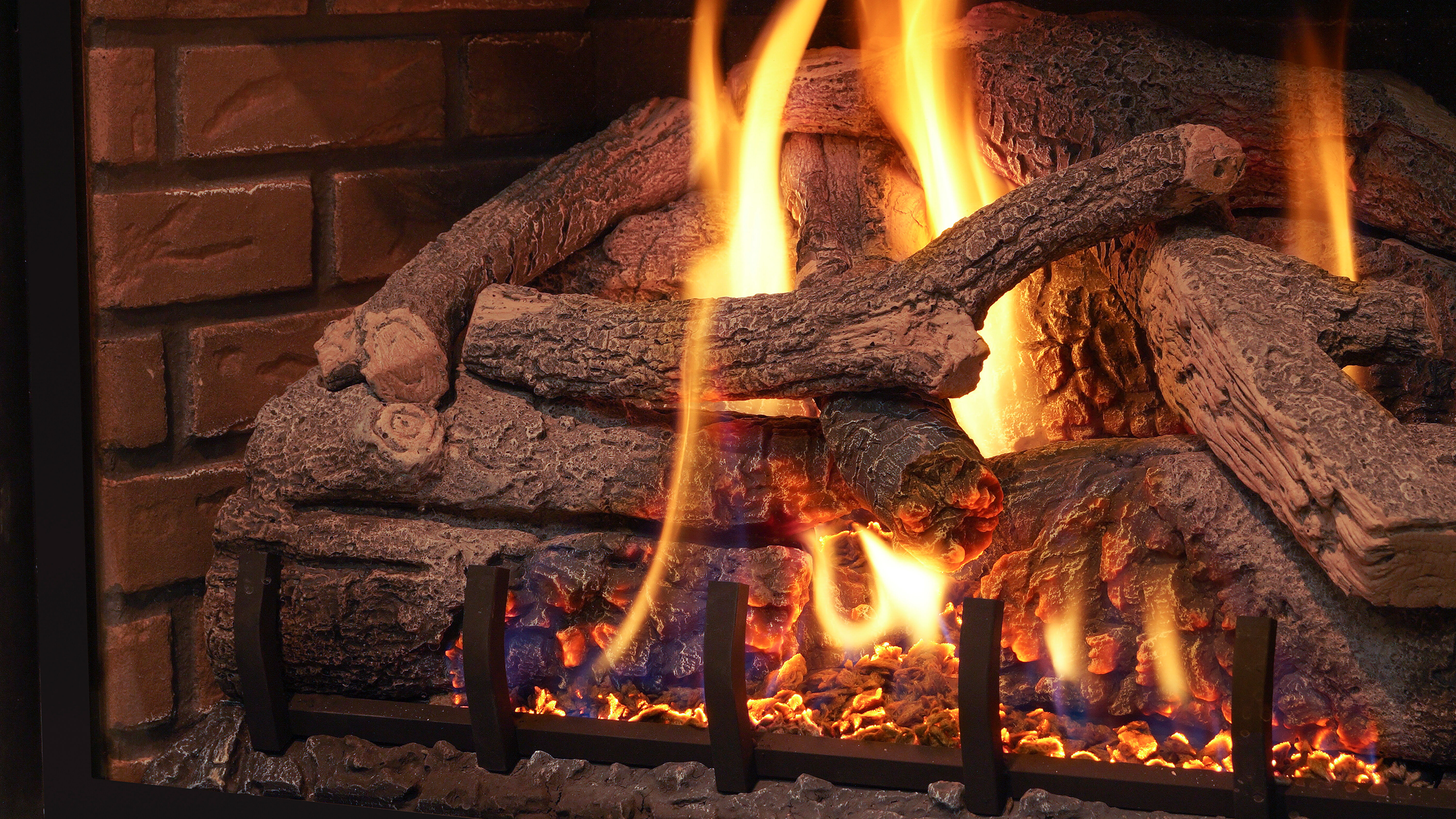 A traditional masonry fireplace with a set of rustic, detailed gas logs burning in the firebox.